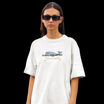 A white t-shirt featuring a playful design of a whale laying on a couch, with the word "Overwhalemed" written above.