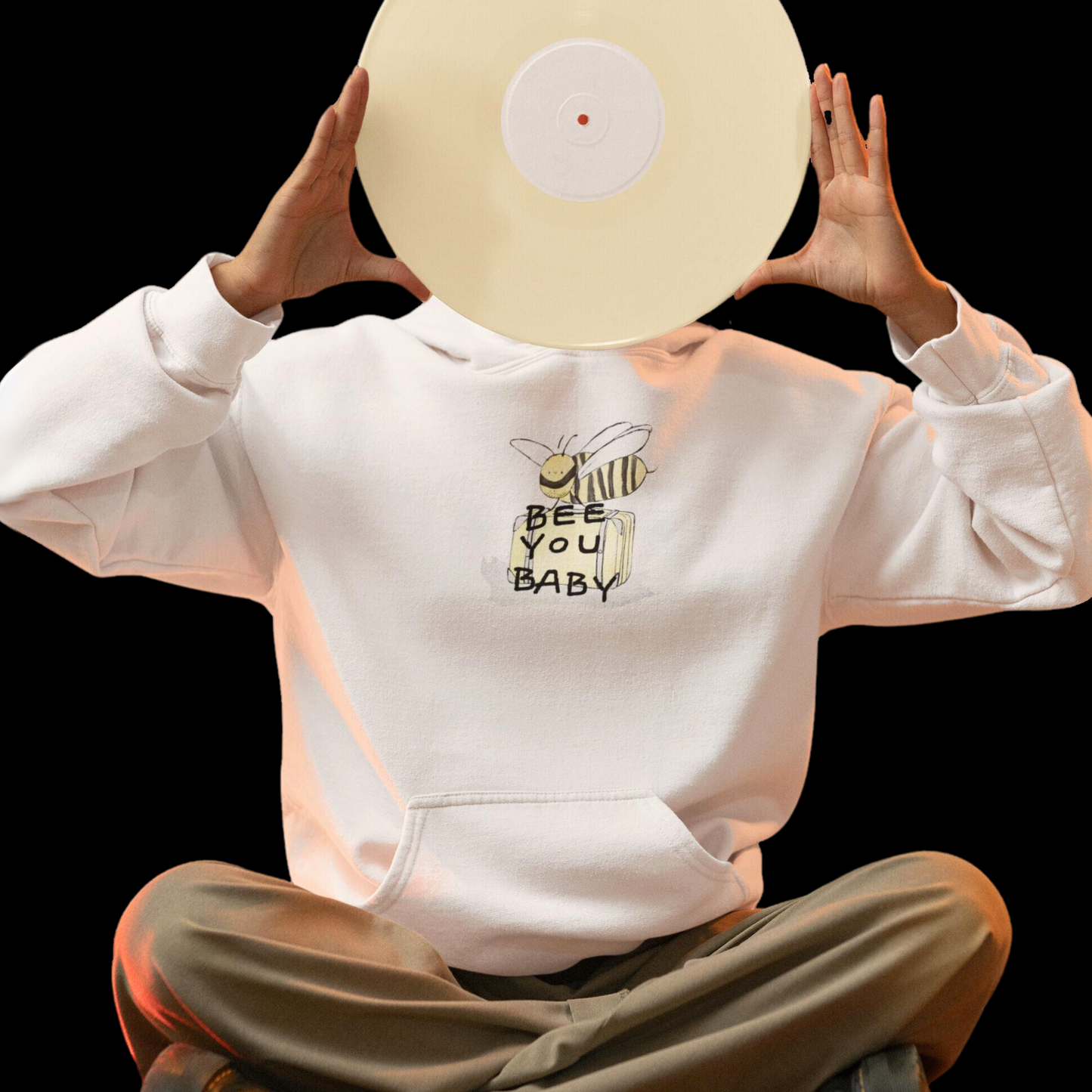 white graphic hoodie with a graphic on the top front of a bee smiling carrying luggage with the words "bee you baby" on top.